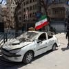 Un homme passe devant un drapeau iranien flottant au-dessus de l'épave d'une voiture dans le centre de Téhéran, le 4 mars 2026. (AFP)